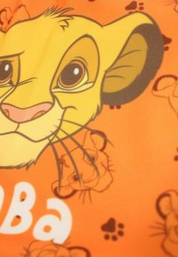 Tissu orange présentant une illustration en gros plan du visage d'un lionceau avec des yeux proéminents, un nez rose et une fourrure jaune. Le texte "Simba" en blanc.