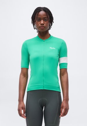 Νέος με πράσινη κοντομάνικη φανέλα ποδηλασίας με λευκή ταινία στο χέρι και σκούρο γκρι επενδεδυμένο σορτς ποδηλασίας.