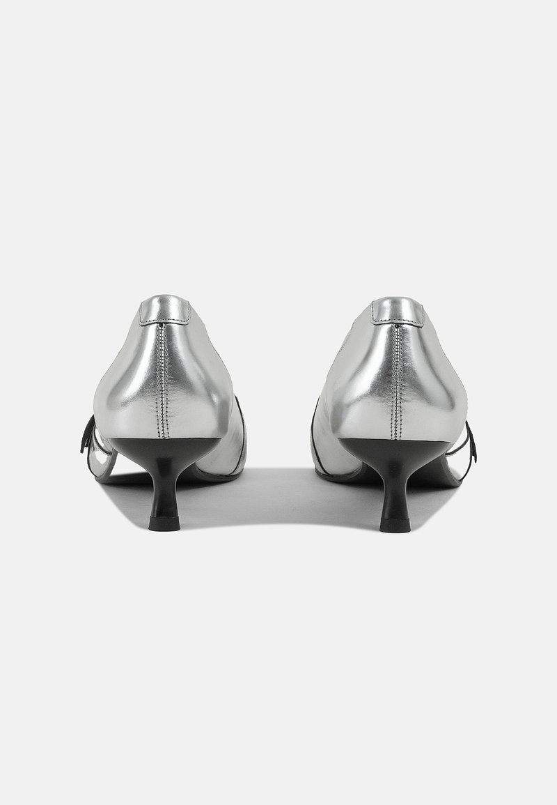 Scarpe in pelle argentata con tacco basso e sottile e punta appuntita. La vista posteriore mostra una texture liscia e accenti minimalisti.