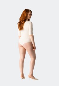 Bodysuit de color crema, con una textura acanalada, manga corta, corte alto en las piernas y cobertura mínima, combinado con mule de tacón beige.