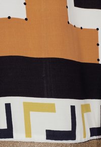 Tessuto multicolore con motivi geometrici marroni, neri e dorati, caratterizzato da una texture liscia e forme contrastanti lungo l'orlo.