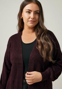 Burgundy stickad cardigan med lös passform, med V-ringning, öppen front och texturerat diamantmönster. Bärs över en svart topp.