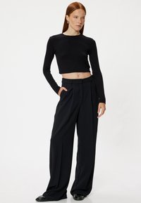 Zwarte lange mouwen cropped top gecombineerd met hoge taille, wijdvallende zwarte broek. Heeft een gladde textuur en een op maat gemaakt ontwerp.