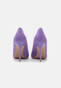 Escarpins en suède violet avec un bout pointu et une fine talon aiguille lavande. Texture lisse et silhouette élégante.