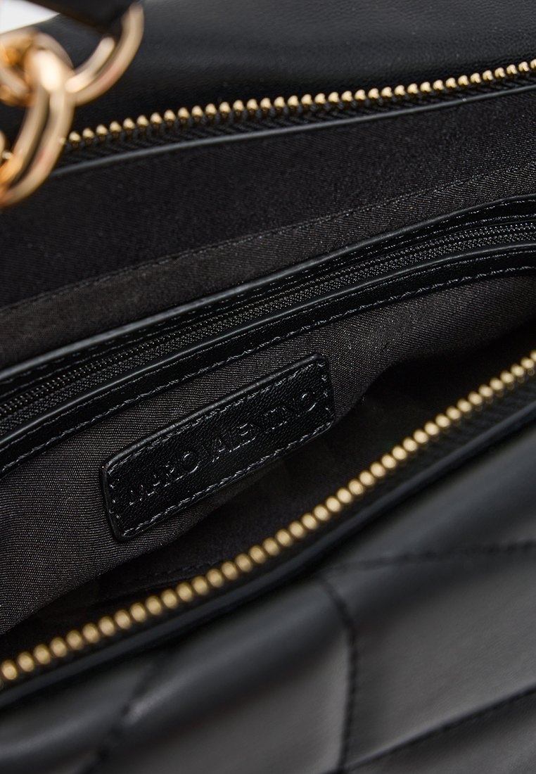 Zwarte gewatteerde handtas interieur met gouden rits en zwart leren label gestikt in de binnenzak.