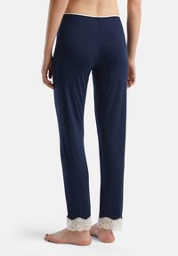 Tmavě modré pyžamové kalhoty vyrobené z měkké látky, s krajkovým lemem na nohavicích a pohodlným elastickým pasem. Volný střih.