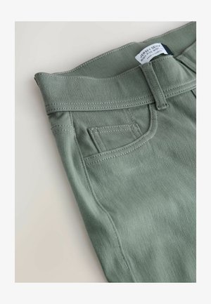 High-waisted green jersey denim jeans with visible stitching, front pocket, and label. Smooth texture and casual design.