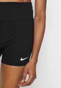 Czarne sportowe spodenki z wysokim pasem, wykonane z elastycznego materiału, z białym logo Nike na dolnej lewej stronie.