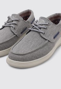 Zapatillas de lona grises con punta redondeada, tejido texturizado, cordones en contraste y una suela ligera. Incluye pequeños detalles decorativos.