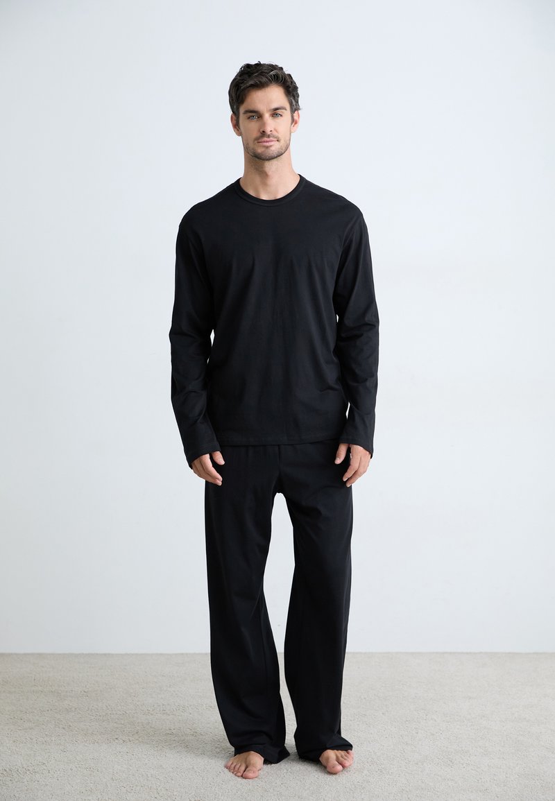Chemise noire à manches longues associée à un pantalon ample assorti, tous deux en tissu doux. La tenue présente un design simple et épuré.