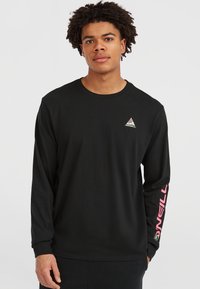 Young man wearing a black long-sleeve shirt with a small triangle logo on chest and pink "O'NEILL" text on right sleeve.