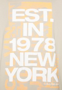 Beige cotton T-shirt featuring large white and orange text reading "EST. IN 1978 NEW YORK.” Smooth texture with a relaxed fit.