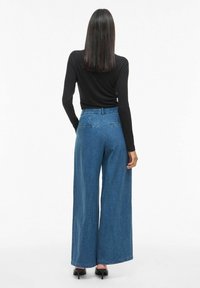 Široke plave traperice visokog struka s pet džepova i glatkom teksturom. Uparene s uskim crnim majicom dugih rukava.