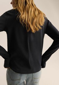 Czarny długi rękaw top o gładkiej fakturze, z zaokrąglonym dekoltem i luźnym krojem, w połączeniu z jasnoniebieskimi dżinsami.