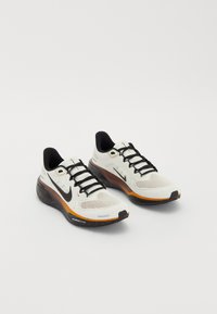 Nike running shoes featuring a white mesh upper, black laces, orange and black sole with speckled detailing, and breathable design.