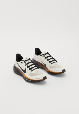 Nike running shoes featuring a white mesh upper, black laces, orange and black sole with speckled detailing, and breathable design.