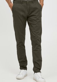 Olive green chinos made of soft cotton material, featuring straight legs, a button closure, and front pockets, paired with white sneakers.