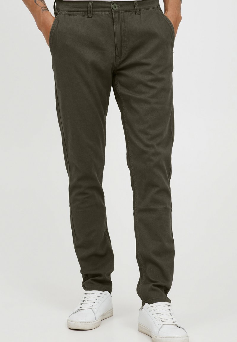Olive green chinos made of soft cotton material, featuring straight legs, a button closure, and front pockets, paired with white sneakers.