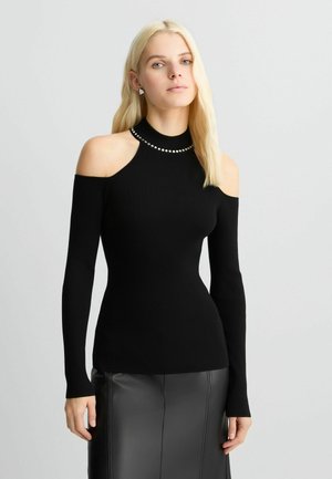 Black ribbed long-sleeve top with cold shoulder design, featuring a high neck adorned with metallic accents. Textured fabric.