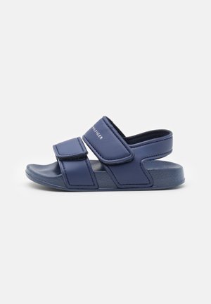 Navy blue slide sandals made of synthetic material, featuring adjustable Velcro straps and a textured footbed for grip and comfort.
