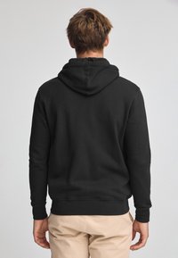 Sudadera de algodón negra con mangas largas, capucha con cordón y puños y dobladillo acanalados. Presenta una textura suave, sin logotipos o patrones visibles.