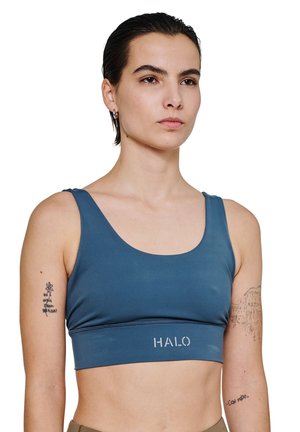 Blå sports-bh med en rund halsudskæring, kort længde og en bred kant med ordet "HALO" i hvidt. Glat stoftekstur.