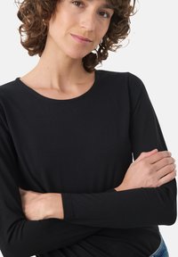 Czarny, długi rękaw, okrągły dekolt, dopasowany krój, miękka tkanina o gładkiej strukturze, bez widocznych wzorów czy dodatków.