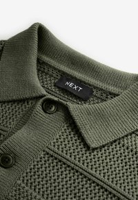 Polo shirt a maglia verde scuro con un motivo testurizzato, dotato di colletto piatto, tre bottoni neri e un'etichetta con la scritta "NEXT."