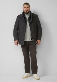 Szary płaszcz z mieszanki wełny z zapięciem na guziki, nałożony na jasnoszary golf, w połączeniu z ciemnobrązowymi spodniami i białymi trampkami.