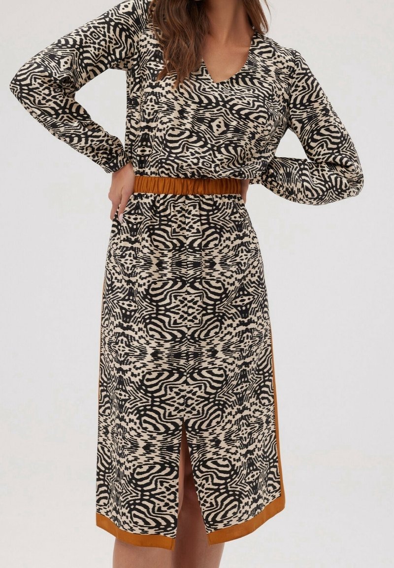 Robe à manches longues avec motif abstrait noir et beige, col en V, ceinture marron et fente au centre de l'ourlet devant.