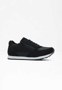 Scarpa sportiva nera con un upper in tessuto testurizzato, una cerniera laterale, suola in gomma e intersuola bianca, caratterizzata da un design lineare.