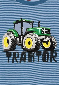 Grün und schwarz gestickter Traktor mit gelben Rädern auf einem blau-weißen gestreiften Shirt-Hintergrund. Der Text lautet "TRAKTOR" unter dem Traktor.