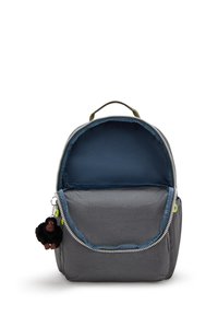 Zaino grigio dalla forma arrotondata, con una cerniera di colore verde e un interno blu. Presenta un charm di una scimmia pelosa attaccato al tirante della cerniera.