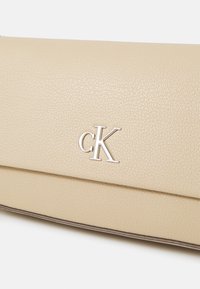 Beige bőr kézitáska texturált felülettel. Ezüst "ck" logóval rendelkezik, letisztult vonalakkal és hajtós záródással.