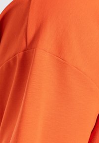 Krátký rukáv košile vyrobená z hladké oranžové tkaniny, se jednoduchým designem a jemnou texturou a švem podél ramene.