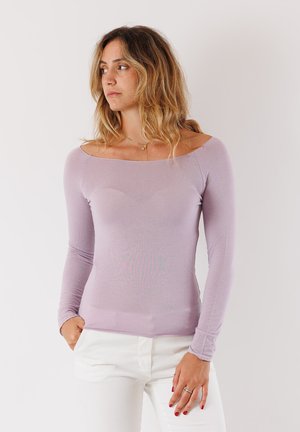 Top a maniche lunghe lilla realizzato in tessuto morbido ed elastico, con scollatura a barca e forma aderente, abbinato a pantaloni bianchi.