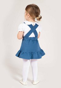 Niebieska bawełniana sukienka z falbaną u dołu, skrzyżowanymi ramiączkami i białą bluzką pod spodem. Dopełnieniem stroju są białe rajstopy i jasne buty.