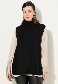 Maglione a collo alto nero in maglia, indossato sopra una blusa in satin beige chiaro, con maniche lunghe e orlo a coste, abbinato a pantaloni in pelle nera.