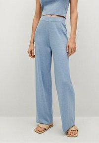 Pantalones elásticos de color azul claro con un ajuste relajado, cintura alta y textura suave, combinados con sandalias planas beige que presentan un acento anudado.