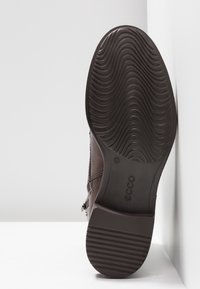 Zapato de cuero marrón con parte superior texturizada, forma curvada, suela de goma con banda de rodadura ondulada y logotipo grabado cerca del talón.