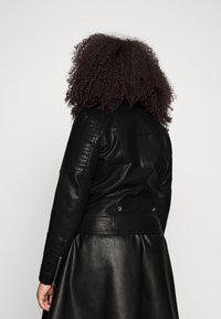 Svart läderbikerjacka med ruggad axeldetaljer, figurnära design och tryckknappsringar, i kombination med en flödande svart läderkjol.