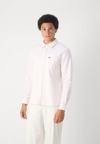 Camicia button-up rosa chiaro con tessuto testurizzato, maniche lunghe e un piccolo logo verde sul taschino sinistro.