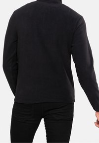 Veste en polaire noire à manches longues, col rond, et texture lisse. Design sans coutures apparentes ni motifs visibles.