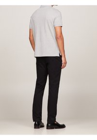 Polo gris à manches courtes avec fentes latérales, assorti à un pantalon noir et des chaussures noires, vu de l'arrière. Tissu lisse et design ajusté.