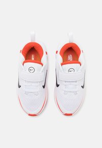 Witte sportieve schoenen met zwart swoosh-logo, rode accenten, ademend bovenwerk van mesh, gevoerde kraag en vetersluiting.
