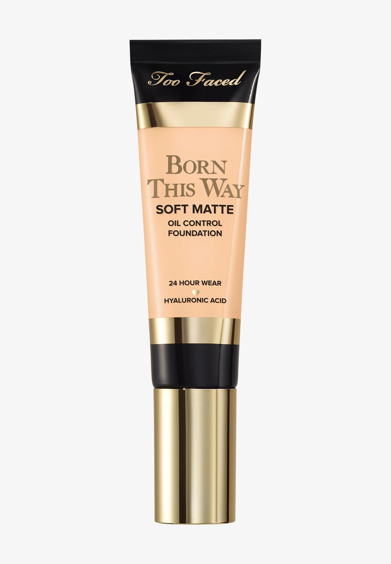 Too Faced Born This Way Soft Matte Foundation in een perzikkleurige tube met gouden accenten en een zwarte dop; omvat details over oliebestrijding en hyaluronzuur.