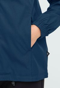 Mornariće plava jakna s elastičnim manžetama, bočnim džepom i malom crnom logotip oznakom. Glatka tekstura i elegantan dizajn.