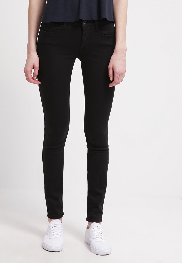 Jeans skinny negros de denim elástico, con una cintura de altura media, cinco bolsillos y un diseño limpio, acompañados de zapatillas blancas.
