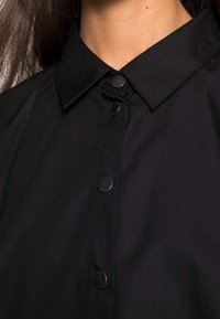 Black button-up shirt featuring a collar, black buttons, and smooth fabric texture, focusing on a close-up view of the neck and placket.