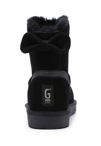 Botín de ante negro con forro interior esponjoso, un lazo prominente en la parte trasera y una suela plana de goma con un detalle de logotipo.